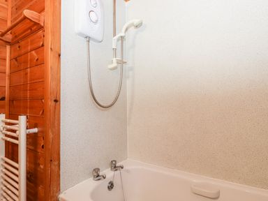 A bathroom with a bathtub shower unit and a wooden wall at Latrigg Lodge Number 9 Burnside Park near Keswick