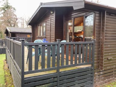 A wooden cabin with a deck that has plastic chairs and a table at Latrigg Lodge Number 9 Burnside Park near Keswick