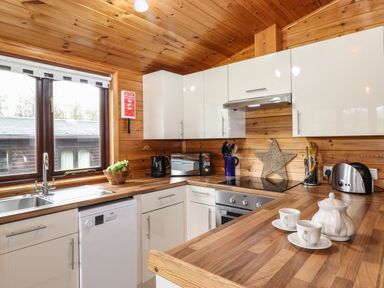 A kitchen with wooden ceiling and countertops white cabinets a sink a kettle a microwave and a tea set on the counter at Latrigg Lodge Number 9 Burnside Park near Keswick