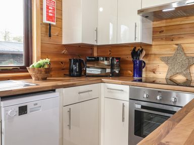 A kitchen corner with wooden countertops a microwave kettle fruit bowl dishwasher oven and woven star on wooden wall at Latrigg Lodge Number 9 Burnside Park near Keswick