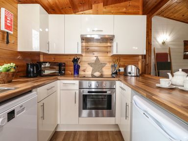 A kitchen with white cabinets wooden countertops and appliances including an oven microwave toaster and kettle at Latrigg Lodge Number 9 Burnside Park near Keswick