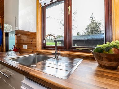 A kitchen sink with a stainless steel faucet and a wooden countertop next to a window with a fruit bowl on the right at Latrigg Lodge Number 9 Burnside Park near Keswick