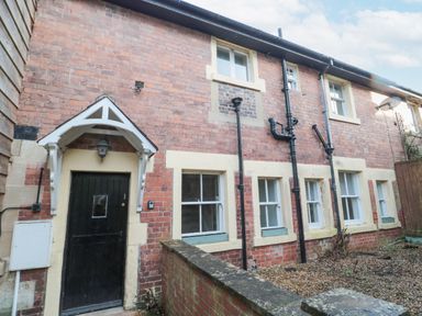 The exterior of a brick house with a black door and multiple windows with cream-colored frames at Courtyard Cottage in Alnwick
