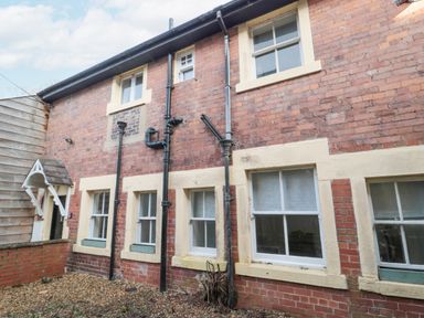 The exterior of a brick building with multiple windows and black drainpipes at Courtyard Cottage in Alnwick