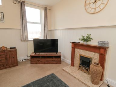 A living room with a television on a wooden stand and a fireplace with decorations at Courtyard Cottage in Alnwick
