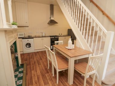 A kitchen and dining area with wooden floor a table and chairs and white cabinetry at Courtyard Cottage in Alnwick