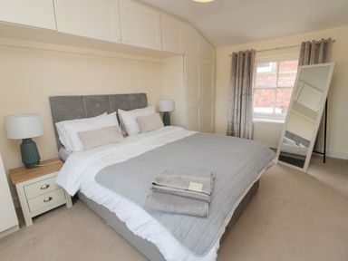 A bedroom with a double bed bedside tables lamps a standing mirror and a window with curtains at Courtyard Cottage in Alnwick