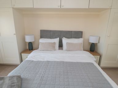 A bedroom with a double bed with gray headboard white pillows beige cushions and bedside tables with lamps at Courtyard Cottage in Alnwick