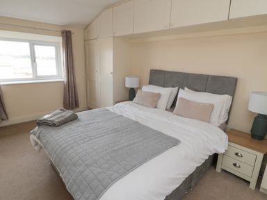 A bedroom with a double bed a window with curtains built in closets and bedside tables at Courtyard Cottage in Alnwick
