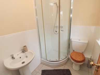 A bathroom with a corner shower enclosure a toilet with wooden seat a pedestal sink and a dark floor mat at Courtyard Cottage in Alnwick
