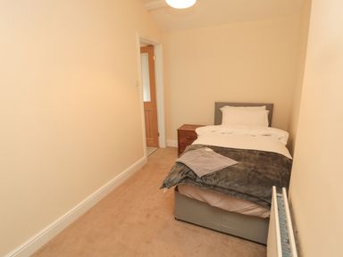 A small bedroom with a single bed beside a wooden nightstand and a radiator on the wall at Courtyard Cottage in Alnwick