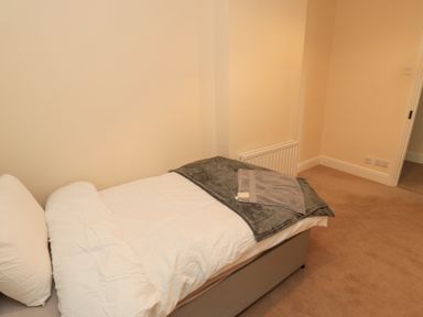 A bedroom with a single bed, white bedding, a gray blanket, and a towel on top at Courtyard Cottage in Alnwick