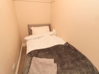 A small bedroom with a single bed white bedding a gray blanket and folded towels at Courtyard Cottage in Alnwick