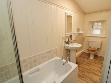A bathroom with a bathtub shower sink toilet and small window at Courtyard Cottage in Alnwick