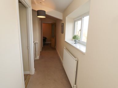 A hallway with beige carpet a radiator under a window and a hanging light at Courtyard Cottage in Alnwick