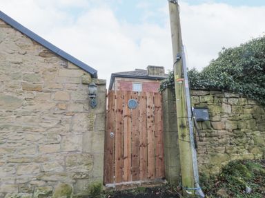 A wooden gate between stone walls with a lamp and a utility pole in front of a house at Courtyard Cottage in Alnwick