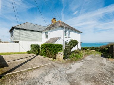 A white two-story house with hedges and a gravel driveway near the sea at Tamarama House in Port Isaac