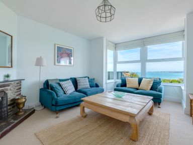 A living room with two blue sofas a wooden coffee table a fireplace and large windows with ocean view at Tamarama House in Port Isaac
