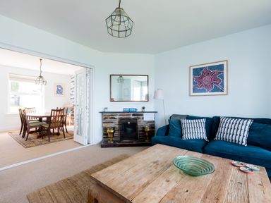 A living room with a blue sofa, wooden coffee table, and fireplace next to a dining table with six chairs at Tamarama House in Port Isaac