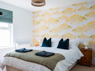 A bedroom with a double bed two dark pillows two folded towels wooden bedside tables and fish patterned wallpaper at Tamarama House in Port Isaac
