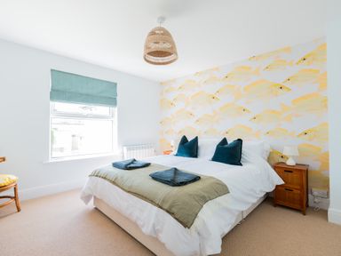 A bedroom with a large bed green throw pillows fish patterned wallpaper and a window with a blue blind at Tamarama House in Port Isaac