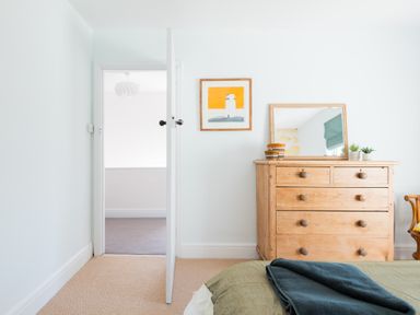 A bedroom with a wooden dresser mirror and plants near an open door at Tamarama House in Port Isaac