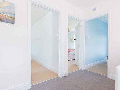 A hallway with three doorways leading to rooms at Tamarama House in Port Isaac