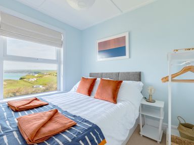 A bedroom with a bed with orange pillows and folded towels near a window with a view at Tamarama House in Port Isaac