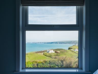A coastal landscape with green fields and a few houses viewed through a window at Tamarama House in Port Isaac