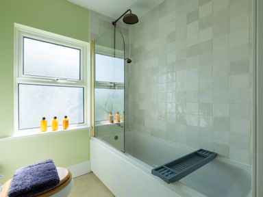 A bathroom with a bathtub shower combination and frosted windows at Tamarama House in Port Isaac