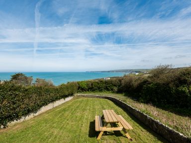 A garden with a wooden picnic table overlooking the sea and coastline at Tamarama House in Port Isaac