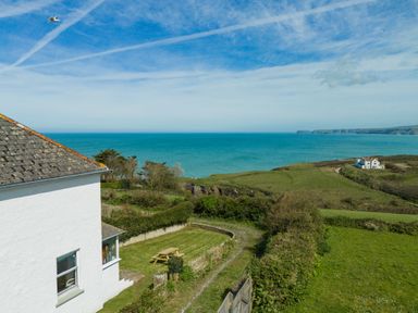A white house overlooking the ocean with greenery and a picnic table at Tamarama House in Port Isaac