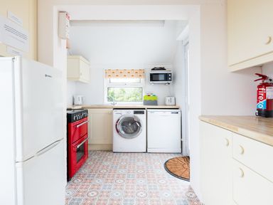 A kitchen with a refrigerator a red oven a washing machine a dishwasher a microwave and a fire extinguisher at Tamarama House in Port Isaac