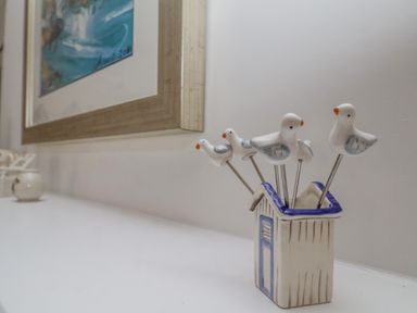 A set of bird-shaped decorative pins in a small house container on a white surface with a framed picture on the wall