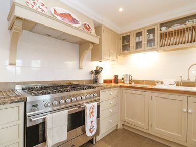 A kitchen with a large stainless steel gas stove beige cabinets and a countertop with kitchen utensils at 9 Church Farm Rise Aldeburgh