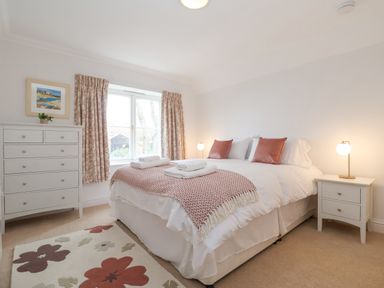 A bedroom with a bed pillows bedside table lamps rug and a chest of drawers at 9 Church Farm Rise Aldeburgh