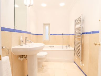 A bathroom with a sink a toilet a bathtub a towel radiator and a small window at 9 Church Farm Rise in Aldeburgh