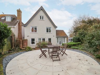 A house with a triangular roof and multiple windows with an outdoor patio table and four chairs on a circular paved area at 9 Church Farm Rise in Aldeburgh