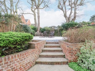 An outdoor garden area with brick steps leading to a patio with wooden chairs and a bench at 9 Church Farm Rise in Aldeburgh