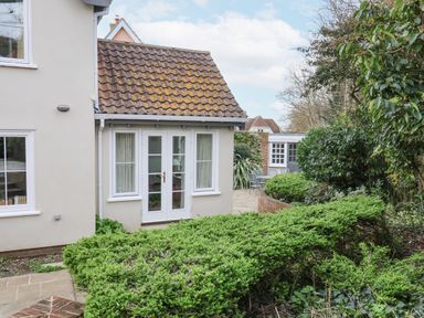 A garden with green bushes and a paved patio with chairs outside a house at 9 Church Farm Rise in Aldeburgh