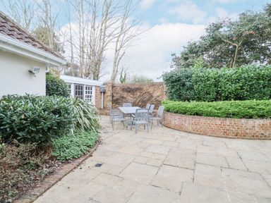 An outdoor patio area with a dining table and chairs surrounded by brick walls and greenery at 9 Church Farm Rise in Aldeburgh