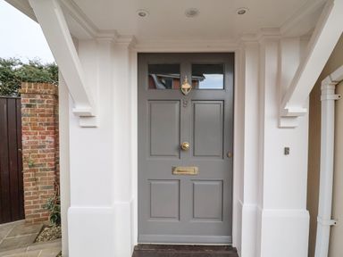 A gray front door with brass fixtures under a white porch at 9 Church Farm Rise in Aldeburgh