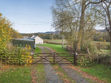 A country driveway with a wooden gate leading to buildings and fields at Country Cottage in Brecon
