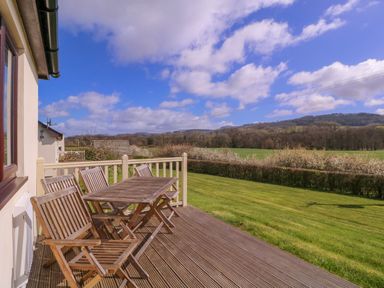 A deck with a table and chairs overlooking a field at Country Cottage in Brecon