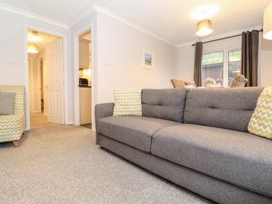 A living room with a gray sofa and patterned armchair near a dining table by a window at Hill Lodge in Applethwaite 2 Limefitt Park near Windermere