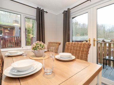 A dining table set with white plates bowls and glasses with wicker chairs and glass doors at Hill Lodge Applethwaite 2 Limefitt Park near Windermere