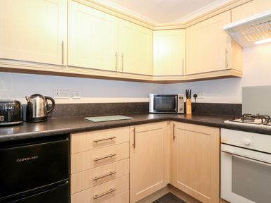 A kitchen with black countertop wooden cabinets microwave kettle toaster knife block and gas stove at Hill Lodge Applethwaite 2 Limefitt Park near Windermere