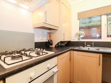 A kitchen with gas stove oven wooden cabinets black countertops and a sink with a window at Hill Lodge in Applethwaite 2 Limefitt Park near Windermere