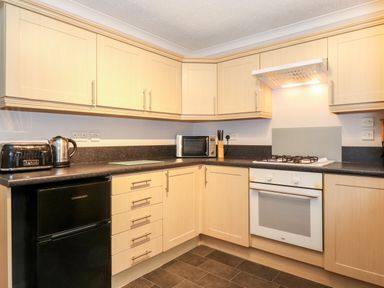 A kitchen with wooden cabinets a black fridge a microwave a kettle a toaster and a gas stove at Hill Lodge in Applethwaite 2 Limefitt Park near Windermere