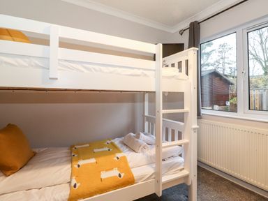 A bedroom with a white bunk bed a yellow blanket and pillows near a window at Hill Lodge Applethwaite 2 Limefitt Park near Windermere